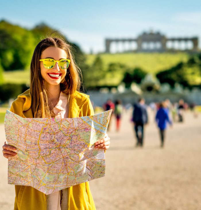 Young female tourist traveling with paper map in Schoenbrunn palace with Gloriette building on the background